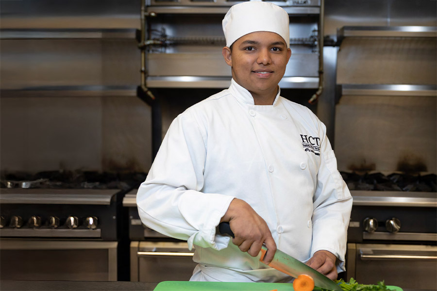 FCC culinary student in white chef coat chopping vegetables in a professional kitchen