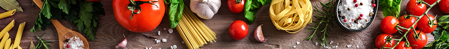 Top view of fresh cooking ingredients including tomatoes, garlic, herbs, pasta, and spices arranged on a wooden surface