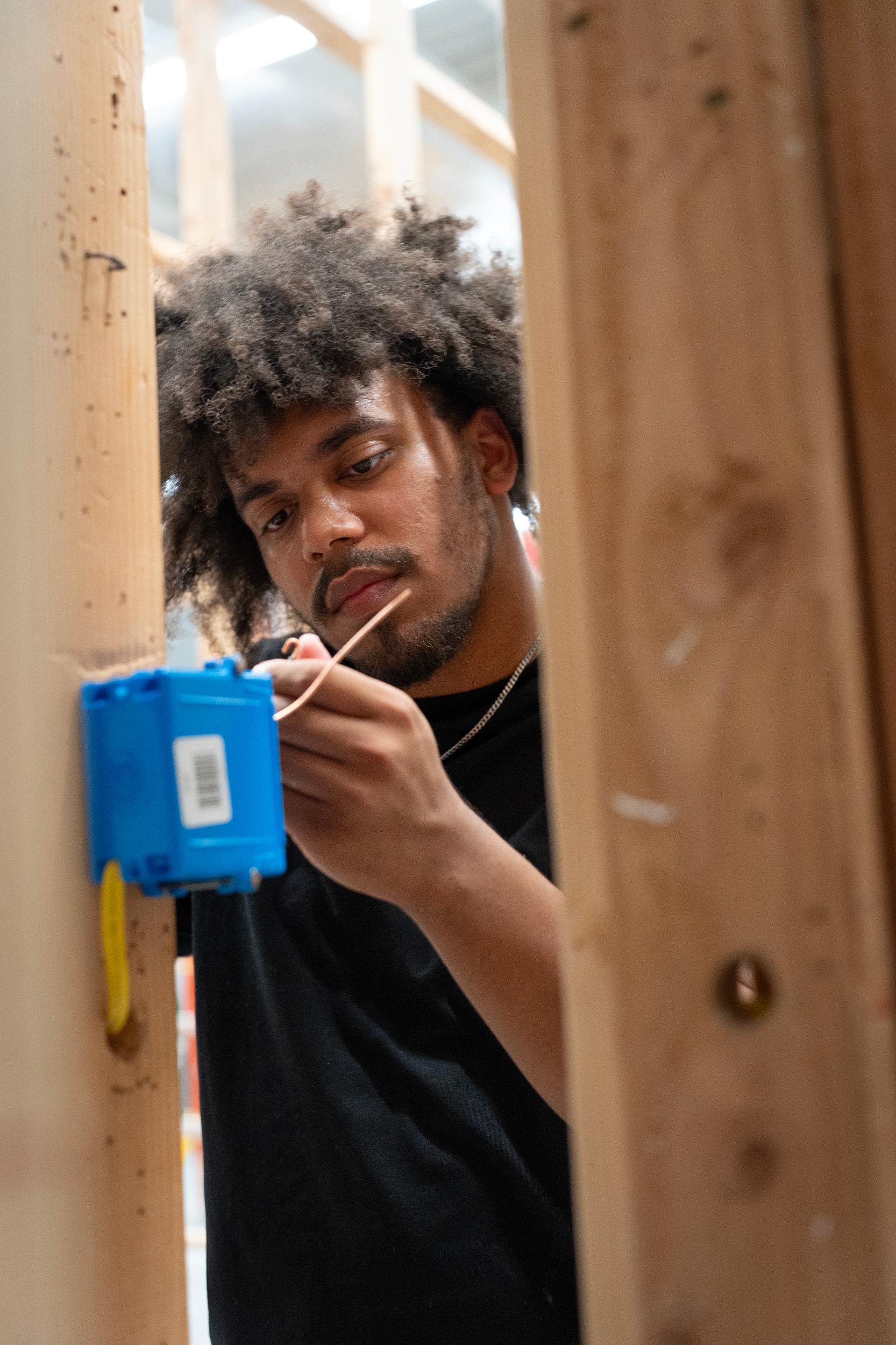 man working on blue electrical box, standing between stud walls